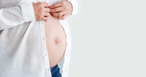 Gestante com a barriga à mostra abotoando uma camisa Gestante com a barriga à mostra abotoando uma camisa