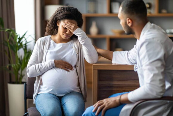 gestante com uma mão posicionada na barriga e outra na testa, olhos fechados e expressão de dor