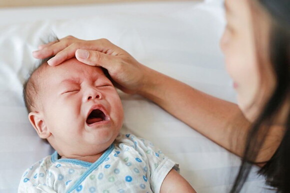 Imagem de um bebê com expressão de choro sendo acalmado pela mãe Imagem de um bebê com expressão de choro sendo acalmado pela mãe