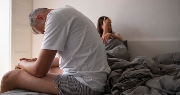 Imagem de um homem sentado em uma cama, parecendo angustiado com a cabeça nas mãos Imagem de um homem sentado em uma cama, parecendo angustiado com a cabeça nas mãos