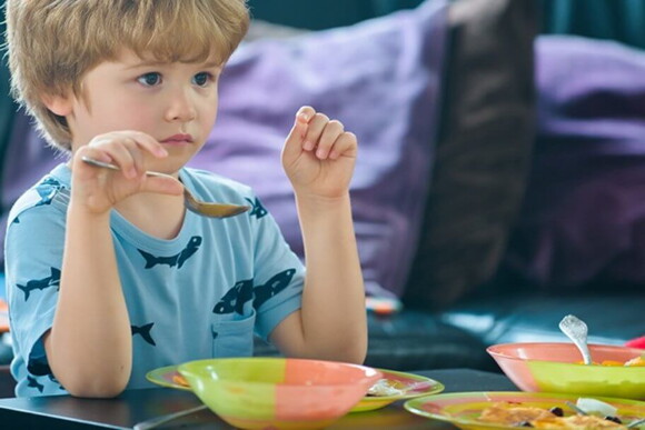Imagem de uma criança segurando uma colher e um prato de alimento