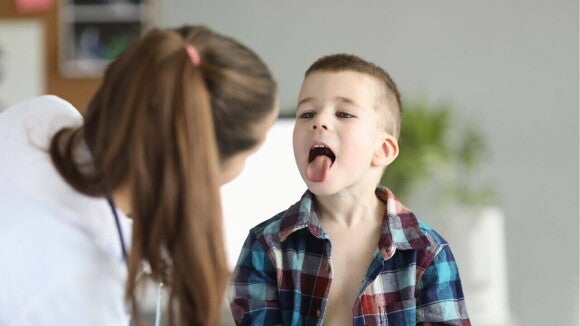 Um menino pequeno está mostrando a língua para uma médica durante uma consulta. Um menino pequeno está mostrando a língua para uma médica durante uma consulta.