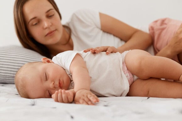 mãe acaricia bebê em cama enquanto ele dorme