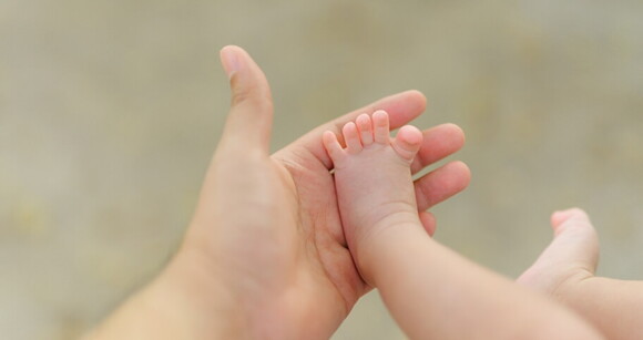 Mão de um adulto segurando delicadamente o pezinho de um bebê