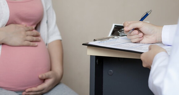 Médico escreve em uma prancheta enquanto uma mulher grávida está sentada à sua frente