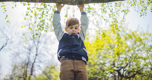 Menino feliz pendurado em um galho de árvore, brincando e explorando o ar livre Menino feliz pendurado em um galho de árvore, brincando e explorando o ar livre