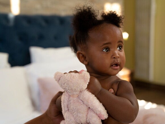 bebê olhando para o lado, segurando um urso de pelúcia