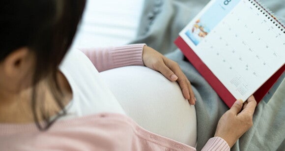 Mulher grávida sentada segurando um calendário Mulher grávida sentada segurando um calendário