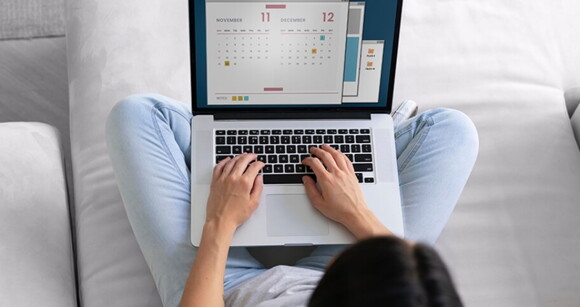 Mulher sentada em um sofá com um notebook aberto em seu colo olhando para um calendário