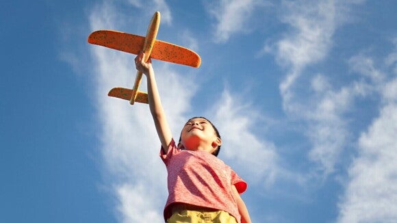 Com o céu de fundo, um menino brinca com um avião vestindo uma camisa rosa. Com o céu de fundo, um menino brinca com um avião vestindo uma camisa rosa.