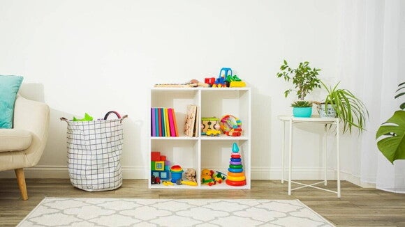 Estante branca com nichos organizados contendo brinquedos infantis coloridos, livros e jogos, ao lado de um cesto de brinquedos e plantas decorativas em um ambiente claro e acolhedor. Estante branca com nichos organizados contendo brinquedos infantis coloridos, livros e jogos, ao lado de um cesto de brinquedos e plantas decorativas em um ambiente claro e acolhedor.