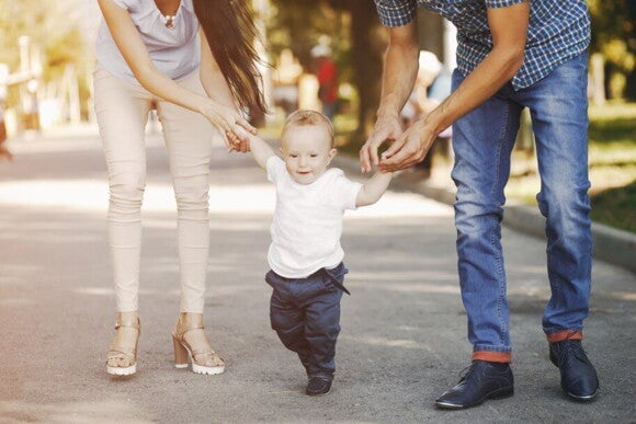 pai e mãe segurando os braços do filho que está dando os primeiros passos pai e mãe segurando os braços do filho que está dando os primeiros passos