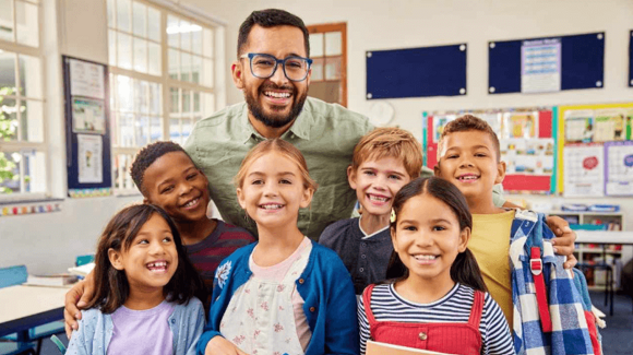 Um professor e um grupo de crianças sorrindo em uma sala de aula.