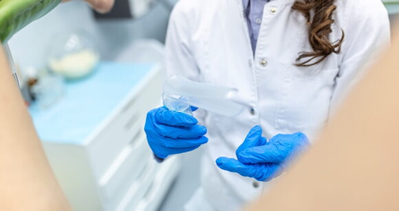 Profissional de saúde segurando um espéculo, se preparando para fazer o exame ginecológico em uma paciente