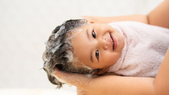 Uma menina sorrindo nos braços de uma pessoa, com uma toalha enrolada no corpo e o cabelo molhado e com espuma Uma menina sorrindo nos braços de uma pessoa, com uma toalha enrolada no corpo e o cabelo molhado e com espuma