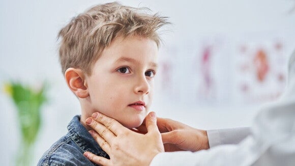 Um menino olha para o lado enquanto um médico toca suavemente seu pescoço e mandíbula.