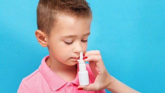Uma mão segurando um spray nasal para uma criança em um fundo azul. Uma mão segurando um spray nasal para uma criança em um fundo azul.