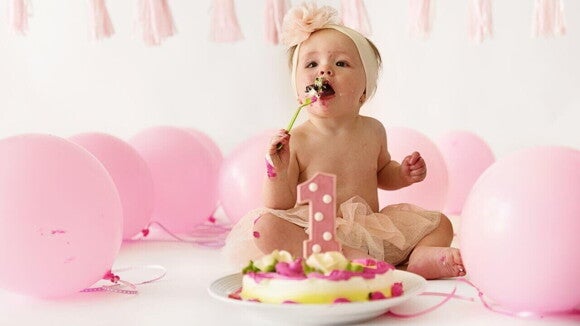 Um bebê comendo um bolo, ao lado de balões de aniversário rosa. Um bebê comendo um bolo, ao lado de balões de aniversário rosa.
