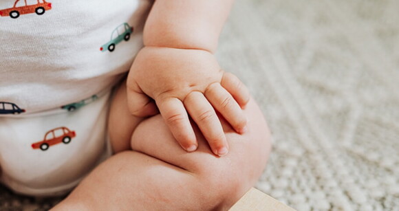 Um adorável bebê sentado no chão com a mão no joelho