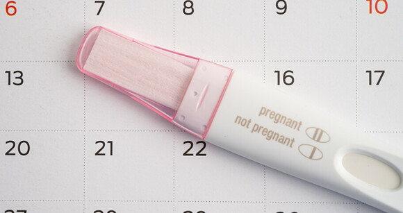 Um teste de grávidez branco e rosa colocado sobre um calendário