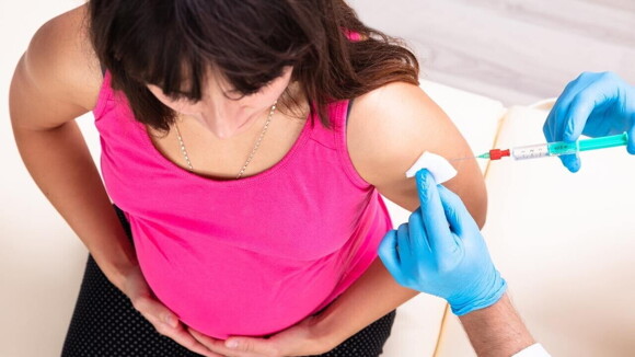 Gestante recebendo a vacina da coqueluche no braço esquerdo por profissional de saúde com luvas azuis Gestante recebendo a vacina da coqueluche no braço esquerdo por profissional de saúde com luvas azuis
