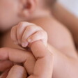 bebê segurando o dedo da mãe enquanto amamenta